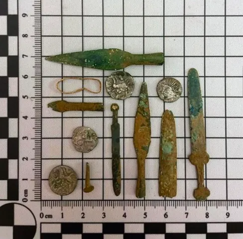 selection of coins, miniature weapons and a gold ring